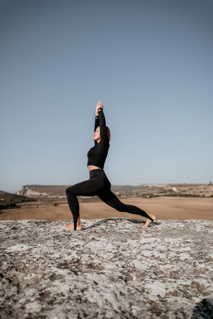Woman in Black Yoga Outfit Practicing Warrior Pose on a Rocky Cliffの写真素材
