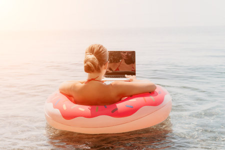 Woman Laptop Beach: Relaxing on a donut float with a laptop in the ocean during a summer day.の写真素材