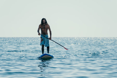 Man Sup Sea. Strong athletic man learns to paddle sup standing on board in open sea ocean on sunny...