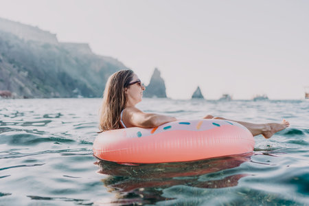 Woman, floating, sea. A young woman relaxing on a donut ring in the ocean with mountains and copy...