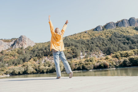 Woman in Yellow Raincoat Raising Arms in Front of a Mountain Lake