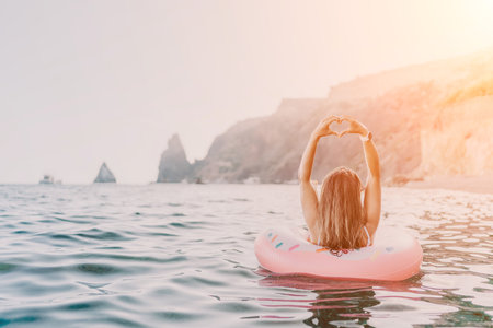 Woman, sea, heart hands. Young woman floating on donut in ocean making heart shape, enjoying summer vacation with copy space.の写真素材