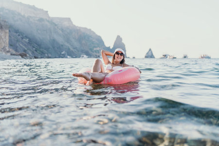 Woman, sea, inflatable. Young woman relaxing on a pink ring in the calm sea near scenic cliffs, enjoying summer vacation.の写真素材