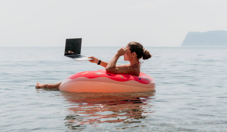 Woman Laptop Float Beach - Working remotely while floating on a pink inflatable ring in the ocean.の写真素材