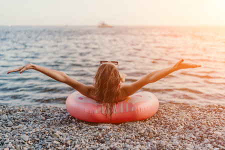 Woman, beach, ocean. A woman relaxes on an inflatable donut on a pebble beach at sunset, feeling freedom.の写真素材