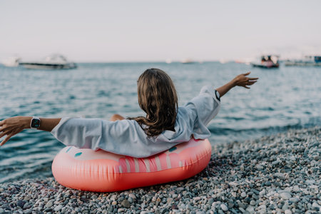 Beach vacation relaxation, person on donut float with outstretched arms on a pebble beach enjoying the seaの写真素材