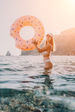 Woman, beach, ocean. Smiling woman holding a donut float in clear sea water with scenic cliffs and copy space.の写真素材