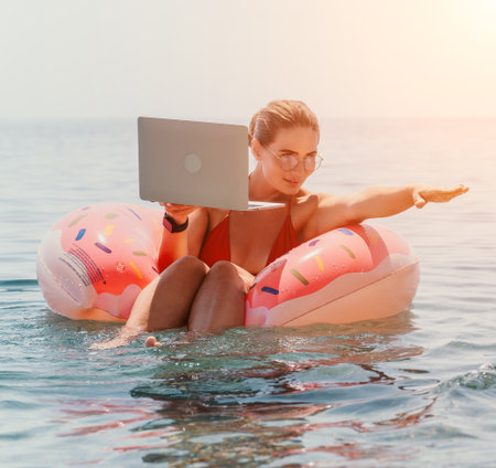 Woman, Laptop, Beach: Working remotely on a donut float in the ocean.の写真素材