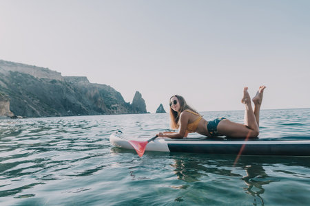 Woman Paddleboard Ocean - Young woman lying on paddleboard in ocean with mountains in background.