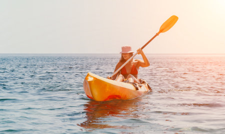 Kayaking Woman Ocean Sunset: Woman paddling yellow kayak on calm water during golden sunset.の写真素材