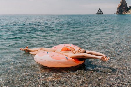 Woman, Inflatable Ring, Sea - Relaxing on a pink inflatable ring in clear sea water near rocky shore.の写真素材
