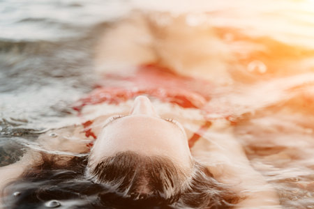 Woman, floating, water. Serene woman relaxes submerged in sunlit spa water, enjoying a peaceful summer vacation.の写真素材