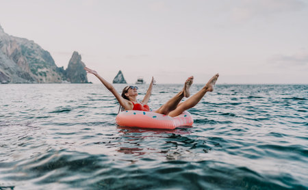 Woman floating sea, enjoying summer vacation on inflatable ring by scenic cliffs.の写真素材