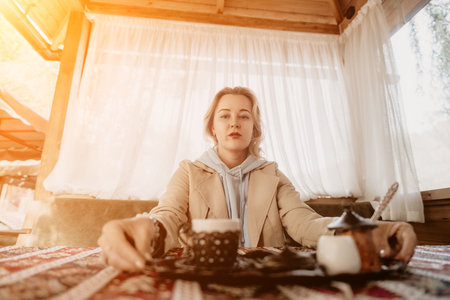 Woman with Blonde Hair in a Beige Coat, Enjoying a Cup of Coffee in a Cozy Cafeの写真素材