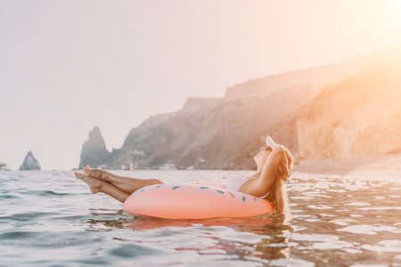 Woman float ocean, happy young woman relaxing on inflatable donut in calm sea with cliffs, summer vacation leisure.の写真素材