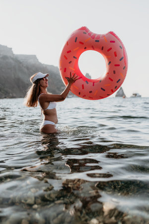 Woman, donut float, sea, smiling woman in white bikini holds inflatable donut in clear water.の写真素材