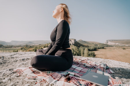 Woman Meditating on a Mountaintop with a Laptopの写真素材
