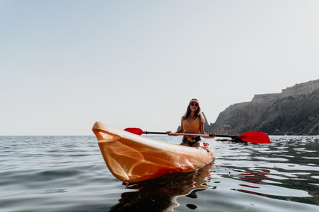 Kayaking Woman Ocean - A woman in a yellow life vest kayaks on the ocean with cliffs in the background.の写真素材