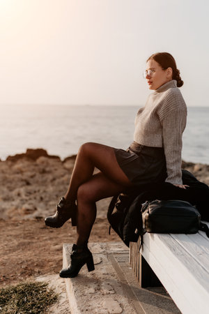 Woman Ocean Coast Sunset: Relaxed woman sits seaside bench enjoying tranquil coastal sunset view.の写真素材