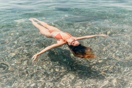 Woman, Sea, Floating - A woman floats on her back in clear blue water with coral beneath her.の写真素材