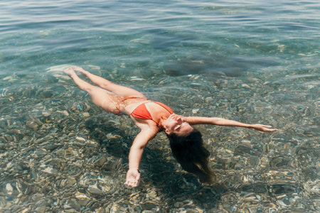 Woman Beach Water - A woman in a red bikini floats on her back in clear water on a beach.