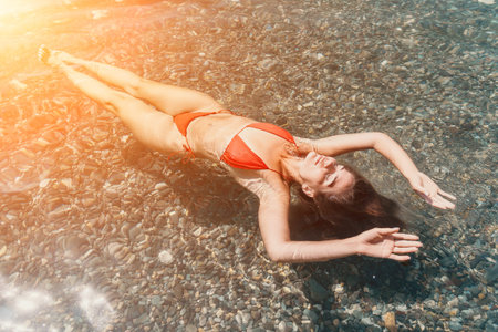 Woman Beach Sunbathing Summer - A woman in a red bikini sunbathes in the shallow water on a beach....
