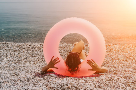 Beach vacation woman relaxing with a pink inflatable ring on a pebble shore during a sunny summer...