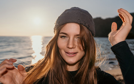 Woman Beanie Sunset Smiling portrait of a young woman wearing a beanie enjoying peaceful golden hour light by the ocean shoreの写真素材