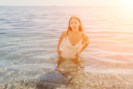 Woman swimsuit sea playful young lady wading in clear ocean water and sticking her tongue out during a golden sunsetの写真素材