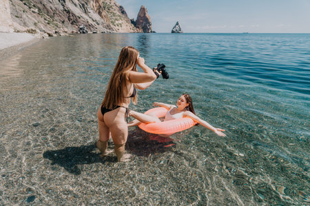 Photographer beach vacation woman taking photos of her friend on a pink inflatable ring in clear...