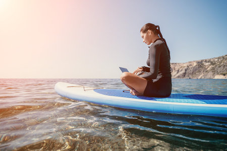 Woman Paddleboarding Laptop Ocean - Working remotely on a paddleboard in the ocean on a sunny day.