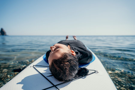 Woman Relaxing Paddleboard Ocean - A woman lays on a paddleboard in the ocean, enjoying a relaxing...