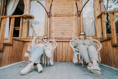 Two Women Relaxing in Hanging Chairs on a Porchの写真素材