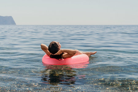 Woman sea swimming relaxing on a pink inflatable ring in calm blue ocean water during a sunny summer...