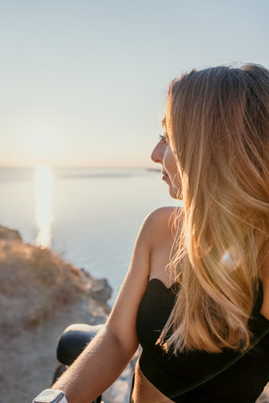 Woman sunset ocean young adult with long blonde hair watching the golden sunset over the calm sea from a rocky cliffの写真素材