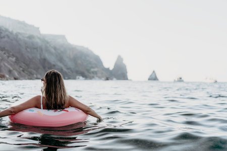 Woman, ocean, relaxation. Young woman floating on inflatable donut in tranquil sea with cliffs, summer vacation copy space.の写真素材