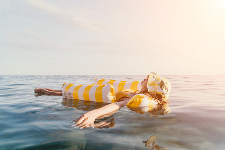 Woman Inflatable Raft Ocean Relaxing - Woman floats on a yellow and white striped inflatable raft in the ocean on a sunny day.の写真素材