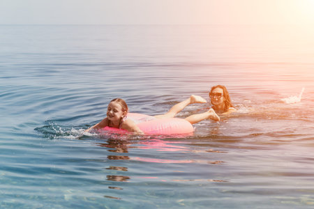 Mother daughter swimming in the sea with a pink inflatable ring enjoying a fun family vacation at sunsetの写真素材