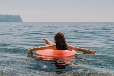 Woman sea inflatable young woman floating on a pink tube while relaxing in calm blue ocean water...