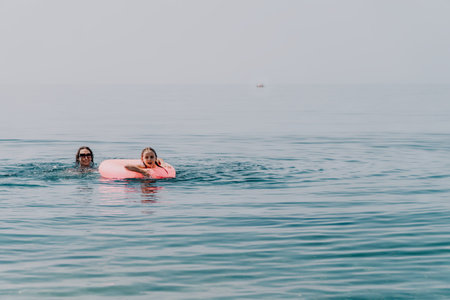 Mother daughter swimming mother and young daughter enjoying a sunny day at the sea with a pink inflatable ringの写真素材