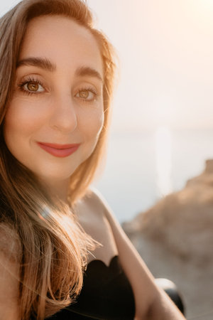 Woman portrait sunset smiling during golden hour on a coast overlooking the sea with warm natural...