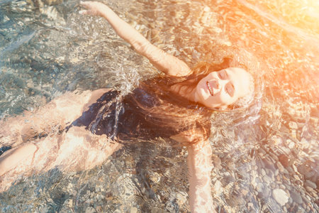 Woman floating water young lady in black swimsuit relaxes in clear sea with rocky bottom under...