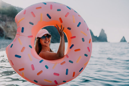 Woman donut sea fun vacation, smiling on inflatable float in ocean at sunset, copy space.の写真素材