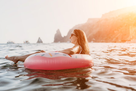 Woman floating donut, enjoying relaxing summer vacation in the sea at sunset