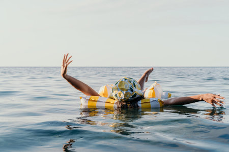 Woman, Inflatable Ring, Ocean - A woman floats on a yellow inflatable ring in the ocean with her...