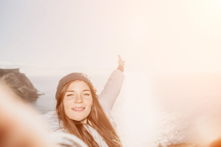 Woman traveler coastal smiling as she takes a selfie on a cliff overlooking the sea during a bright...