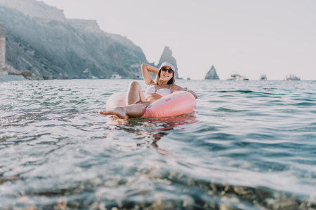 Woman, relaxing, summer vacation on inflatable ring in clear sea with scenic mountains.