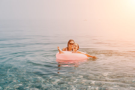 Vacation family swimming mother and daughter enjoy playing with a pink inflatable ring in the clear...