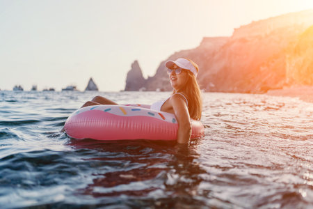 Woman, beach, vacation. Happy woman floating on inflatable donut ring in calm sea with cliffs, copy...