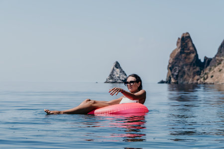 Woman relaxing floating on pink inflatable ring in calm sea water enjoying summer vacation near scenic rocky coastline cliffsの写真素材